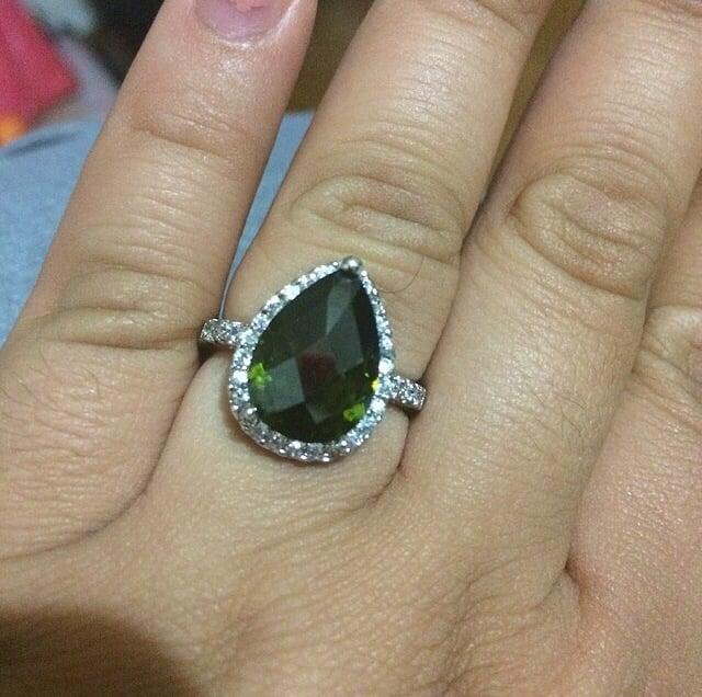 White gold ring with large pear-cut green gemstone and halo of stones